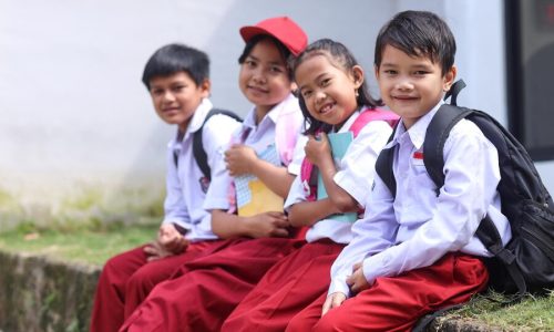 elementary-school-students-with-backpacks-wearing-uniform-sitting-looking-camera-smiling_603656-3671